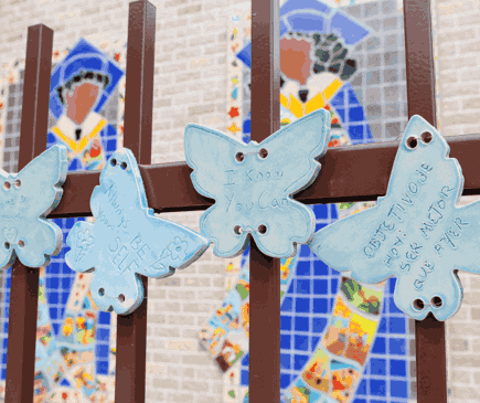 Photo of graduation tile mural on the side of a wall behind a fence with ceramic butterflies