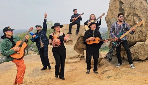 The Group El Santo Golpe on top of a rock formation outside playing their isntruments